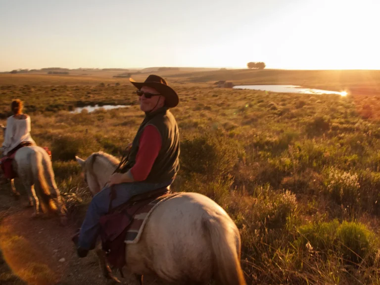Jinetes en caballos criollos por el campo uruguayo al atardecer, paisaje del interior del país como el de Durazno, Uruguay