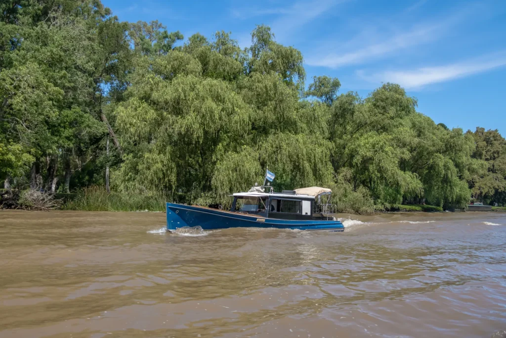 Río de aguas marrones con sauces y una lancha en la cuenca del Plata, paisaje fluvial como el del río Uruguay en Fray Bentos