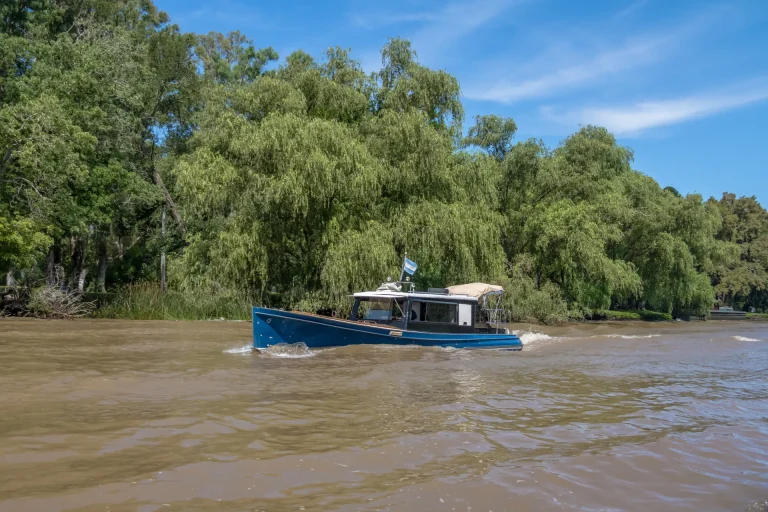 Río de aguas marrones con sauces y una lancha en la cuenca del Plata, paisaje fluvial como el del río Uruguay en Fray Bentos