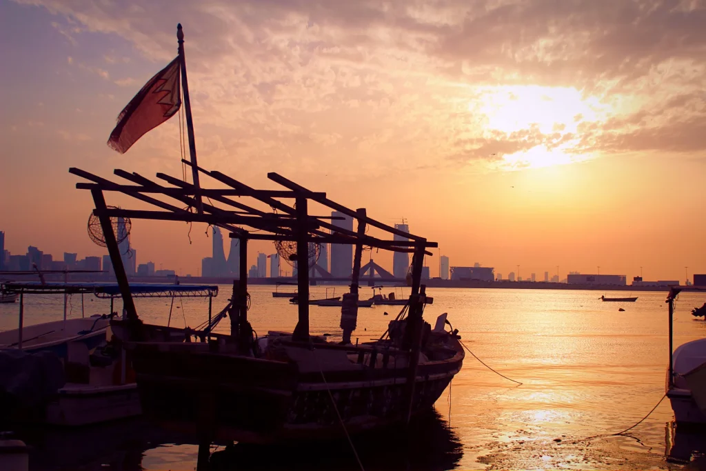 Barco tradicional con la bandera de Baréin frente al horizonte de Manama al atardecer