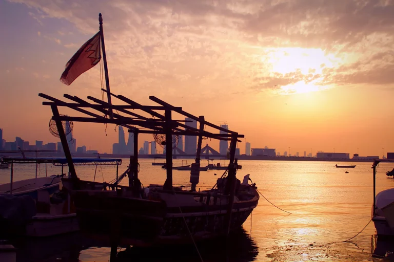 Barco tradicional con la bandera de Baréin frente al horizonte de Manama al atardecer
