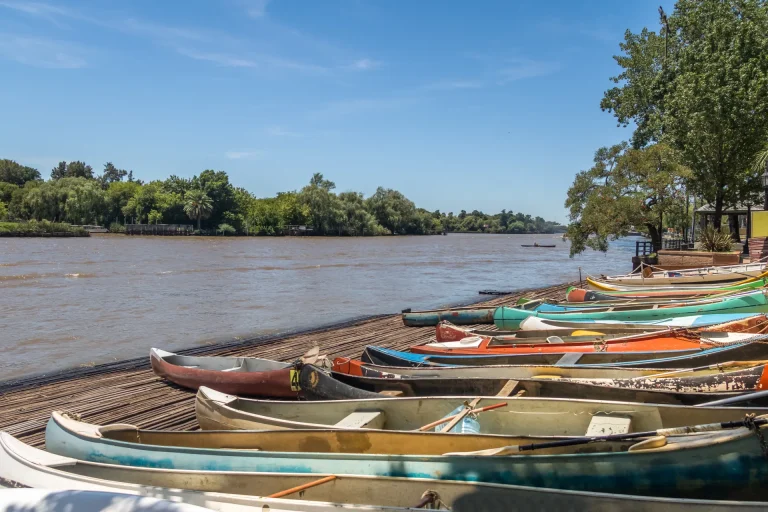 Botes de remo a orillas de un ancho río rioplatense, paisaje similar a la costanera del río Uruguay en Paysandú