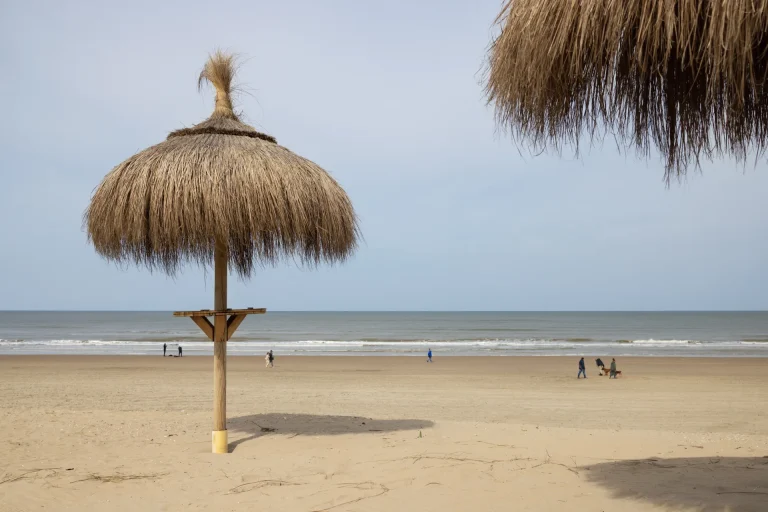 Sombrillas de paja en una playa de arena soleada, ambiente similar a Punta Sal, Perú